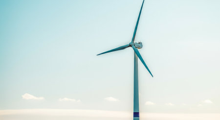 Wind turbine is standing tall in the sky. The wind turbine is blue and whiteの素材