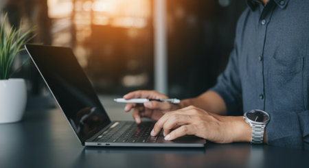Man is typing on a laptop computer. He is holding a pen in his hand. The laptop is open and the screen is blackの素材
