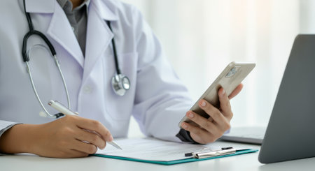 Doctor is writing on a clipboard with a pen. A cell phone is on the table next to the clipboardの素材