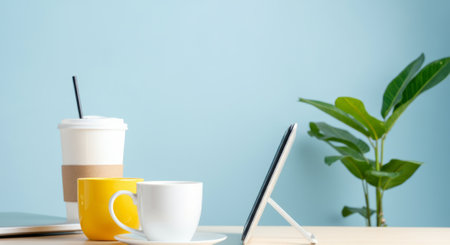 Yellow coffee cup sits on a table next to a white cup. A tablet is on a stand in front of the white cupの素材