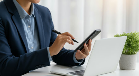 Man is sitting at a desk with a laptop and a pen. He is writing on the laptopの素材
