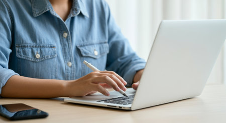 Woman is typing on a laptop computer. She is using a pen to write on the laptopの素材