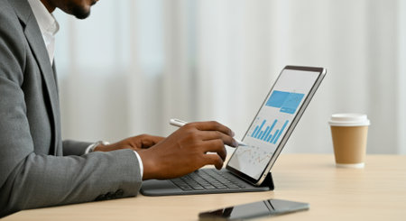 Man is typing on a laptop with a pen. The laptop screen shows a graph. There is a cup of coffee on the tableの素材