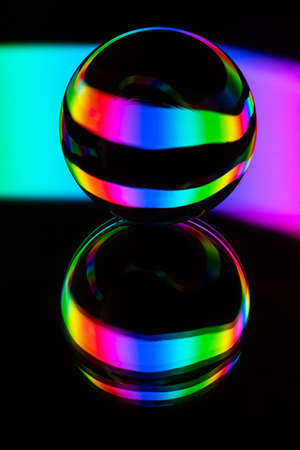 Glass crystal ball on a mirror surface with a rgb multicolor pattern light painting fractals on a...
