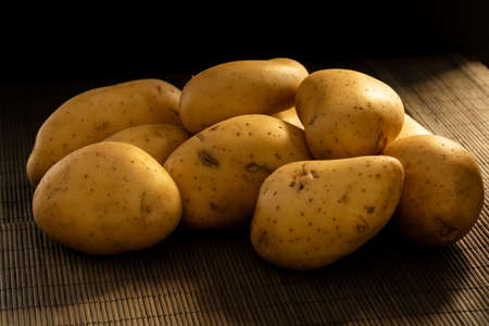 A bunch of potatoes on a wooden tablecloth in a dark sceneの写真素材