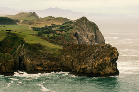 Beautiful landscape of a green field and wavy cliff with mountains on the background in north Spain