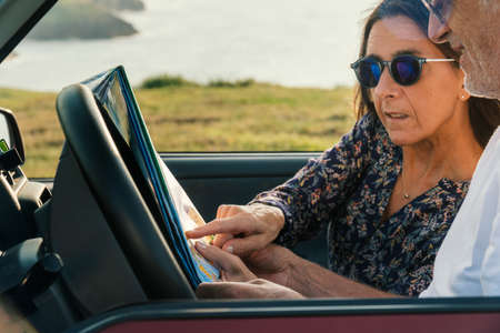 Aged Couple pointing at the map and traveling through the coast in their 4x4 convertible car