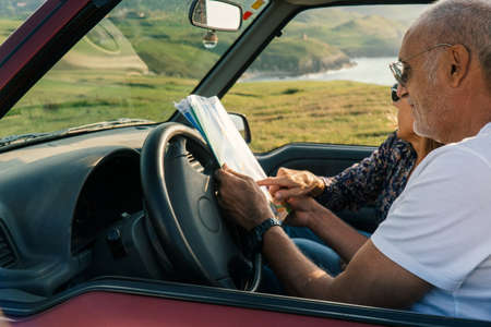 Aged Couple watching a map through the coast in their 4x4 convertible car