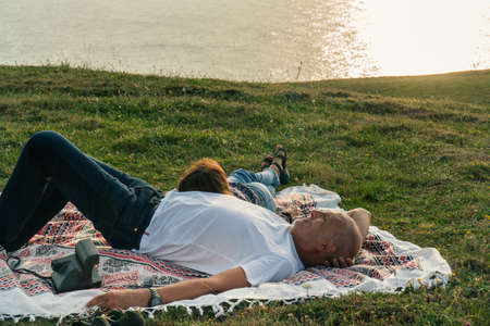 Aged Couple laying on the meadow and enjoying the sunset on the coast