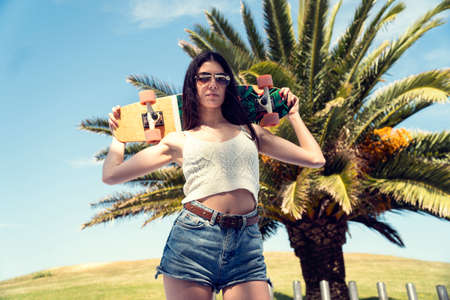 Skater girl posing with her skateboard with palms on the background