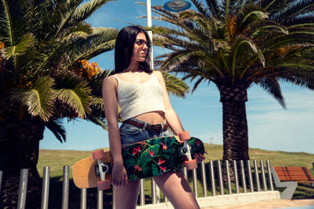 Skater girl posing with her skateboard with palms on the background
