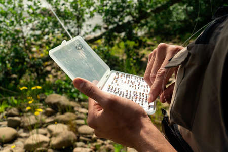 Young man choosing the hook for fishing trouts in the river