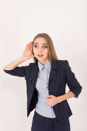 I love gossips! Surprised young businesswoman in suit holding hand near ear while standing against...