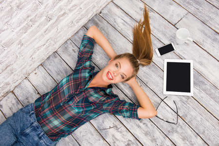 Top view of young woman lying on the floor with tablet and phoneの写真素材