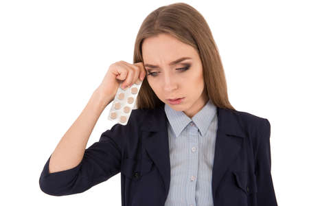 Feeling headache. Frustrated young woman in formalwear touching head with fingers and holding headache tabletsの写真素材