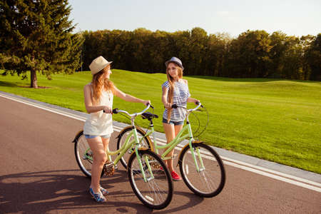 two pretty happy  girls  walking with a bicycle on parkの写真素材