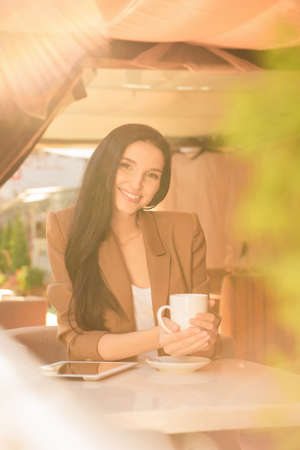 pretty girl sitting in a cafe on the terrace with a cup of coffeeの写真素材
