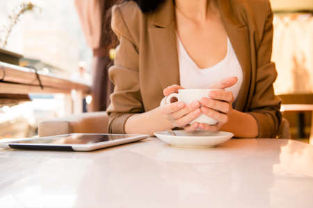 young woman holding cup of coffee in cafe with tablet