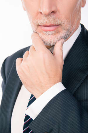 intelligent businessman with gray beard ponders putting his hand on chinの写真素材