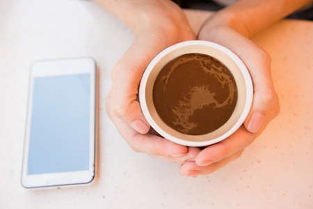 top view of  woman holding cup of coffee in cafe near phone on tableの写真素材