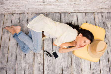 top view of pretty girl in anticipation of traveling and sleeping on a suitcaseの写真素材