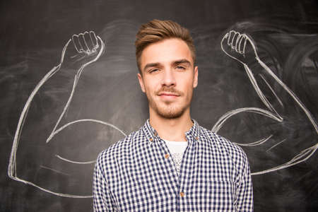 Young  man against the background of depicted muscles on chalkboardの写真素材
