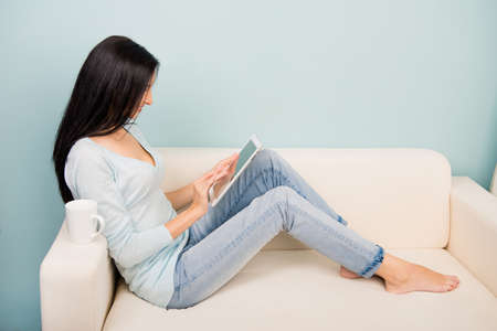 Young woman with a cup holding tablet  sitting on the sofa