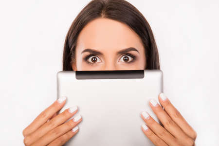 Frightened young woman hiding face behind the tablet