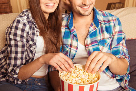 happy loving couple eating popcorn on the couchの写真素材
