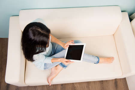 Cute young woman holding tablet sitting on the sofaの写真素材