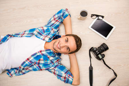 Top view of man lying on the wooden floor with camera, coffee and phoneの写真素材