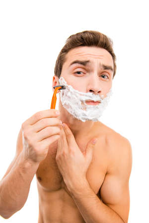 Handsome young man with shaving foam on his face and razorの写真素材