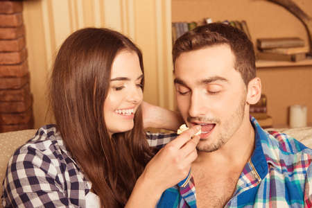 loving girl feeding her boyfriend popcorn on the couchの写真素材