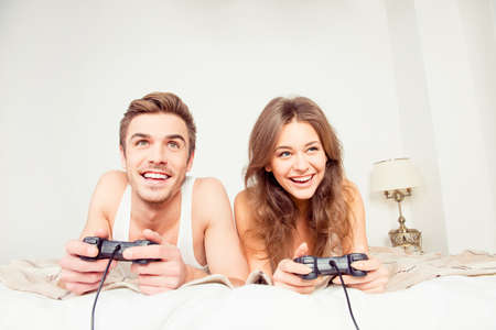 Happy couple in love playing video games with joysticks on the bed