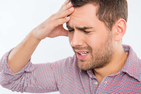 Handsome young man touching his head with one hand feeling strong headache, close up photo