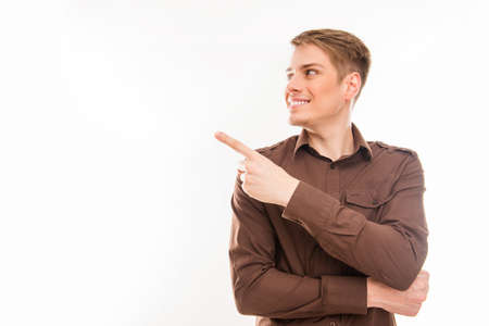 Pretty  young smiling man in brown shirt gesturing and pointing awayの写真素材