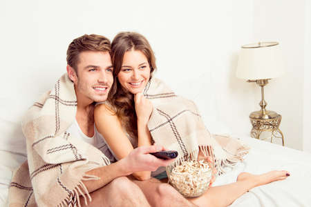 Young beautiful couple in love at home under plaid with popcornの写真素材
