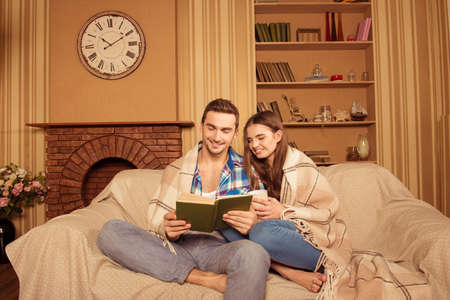 Happy couple in love with plaid reading book on the sofaの写真素材