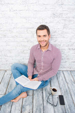 Young man sitting on the floor with book and cup of coffee