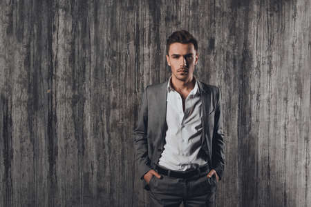 Handome man in suit on the grey background with hands in pocketsの写真素材