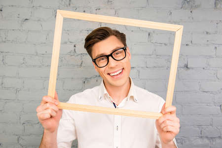 Cheerful happy man in glasses holding wooden frameの写真素材