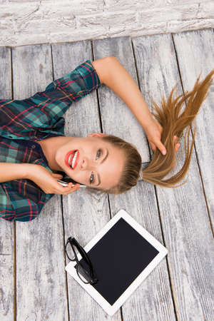 Pretty woman lying on floor with tablet and glasses and talking on phoneの写真素材