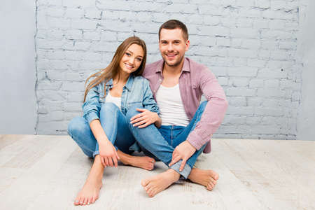 Happy pretty man and woman sitting barefoot on the floorの写真素材