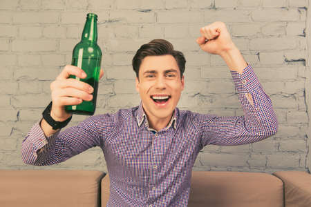 Smiling fan watching footbal with beer and raised fistの写真素材