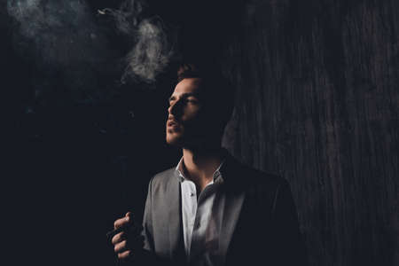 Successful businessman with cigar and smoke on black background