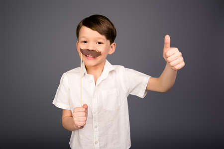 Cheerful little boy with paper mustache showing thumb upの写真素材