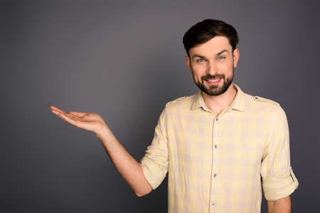 Smiling young man offering a product on gray backgroundの写真素材