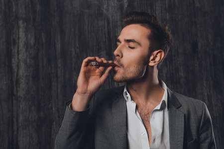 Handome brutal man in suit on the gray background smoking a cigarの写真素材