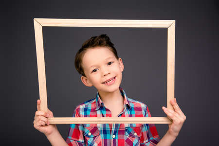 Cheerful young little boy holding wooden frameの写真素材