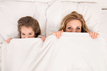 Top view of comic woman and her daughter hiding faces behind blanketの写真素材